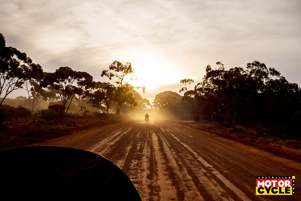 Motorbike riding into the sun following another bike on dusty dirt road