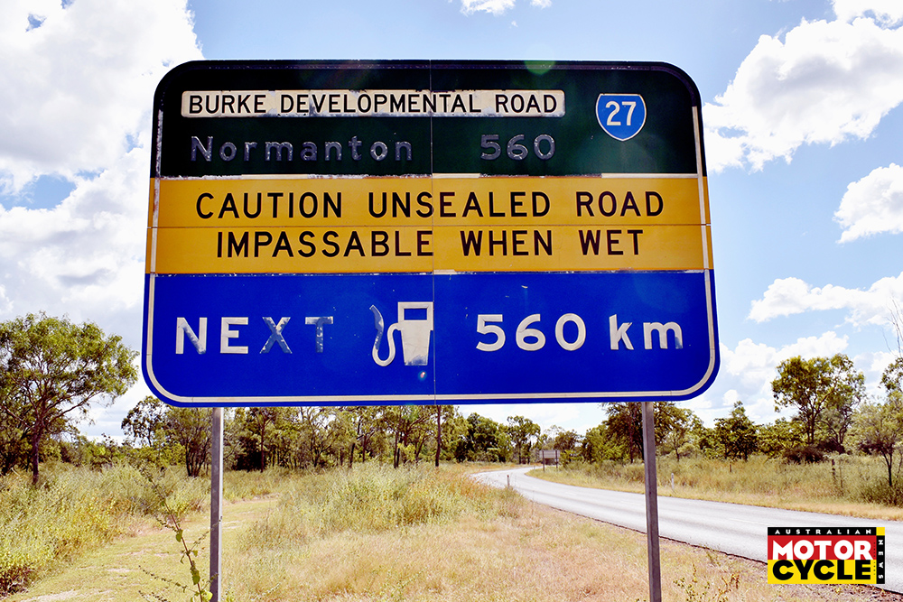 A neglected sign in outback Australia indicating an unsealed road with next fuel station 560 kilometers away